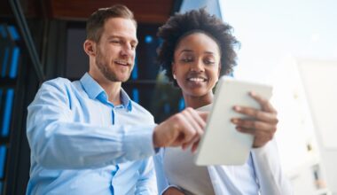 Two investors look at something on a tablet outdoors.
