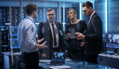 People speaking in dimly-lit room with servers in the background.