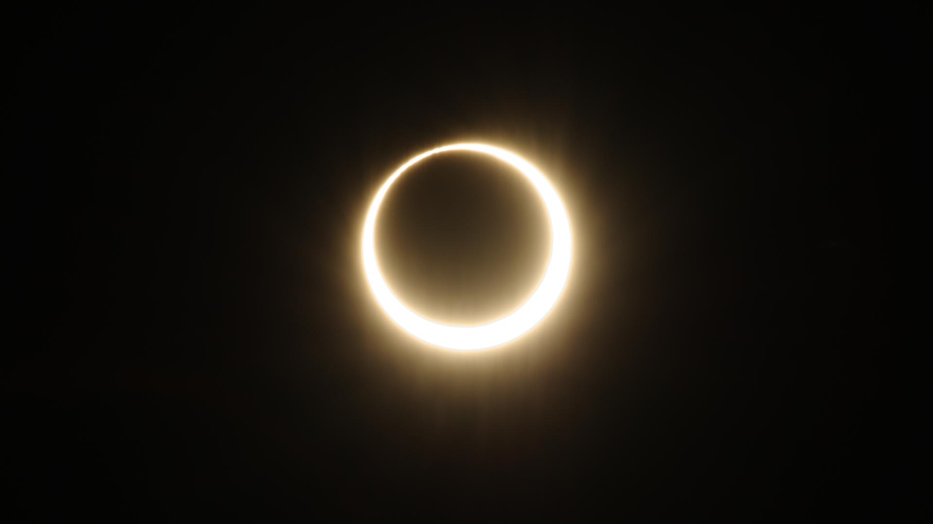 The moon's silhouette is surrounded by the outer edge of the sun in a black sky during an annular solar eclipse.