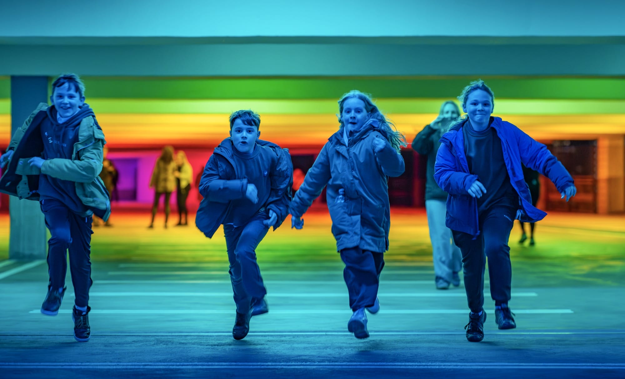 children run amid chromatic light blanketing a parking garage by Liz West