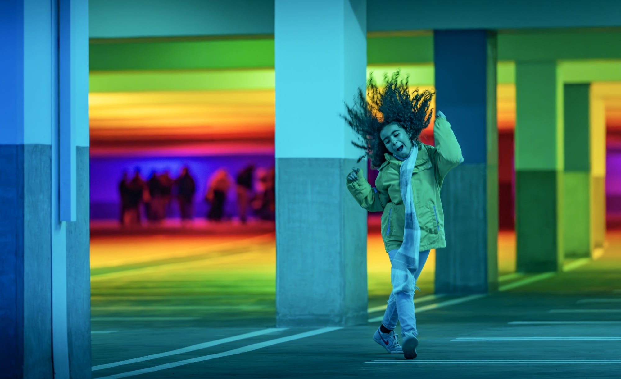 a child dances amid chromatic light blanketing a parking garage by Liz West