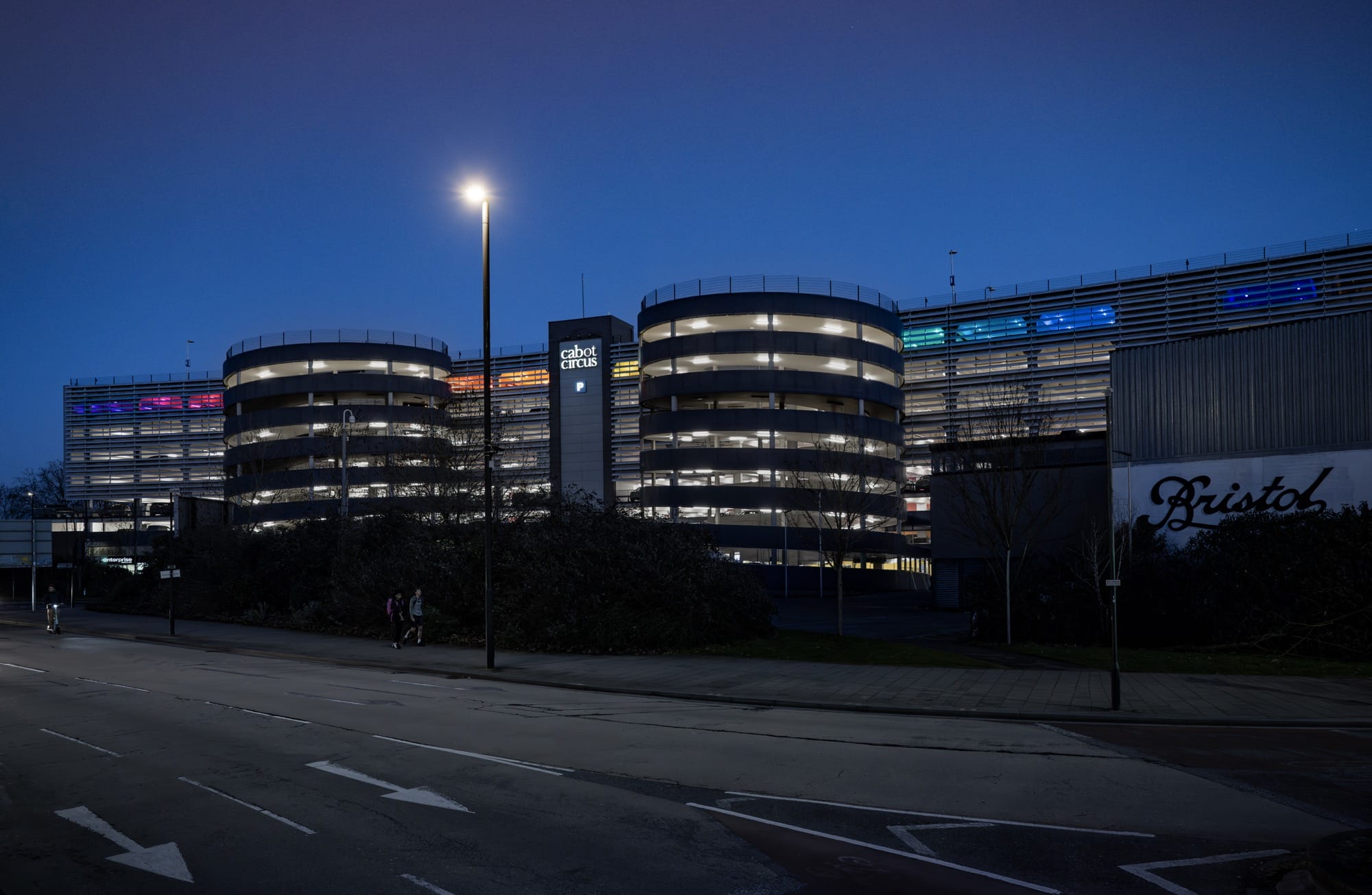 a single floor of a parking garage is illuminated by colorful light by Liz West