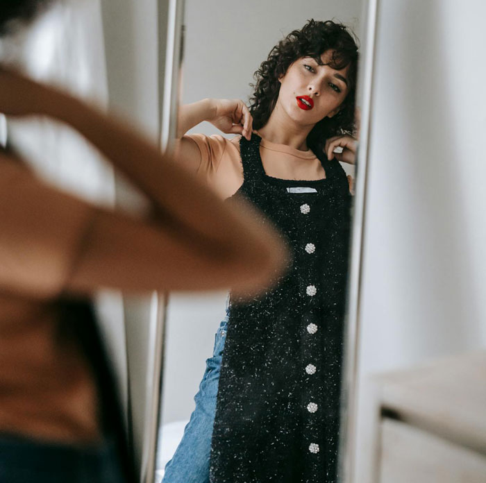 Woman looking frustrated in mirror, holding dress, reflecting emotions related to parenting and family conflict. Woman looking frustrated in mirror, holding dress, reflecting emotions related to parenting and family conflict.