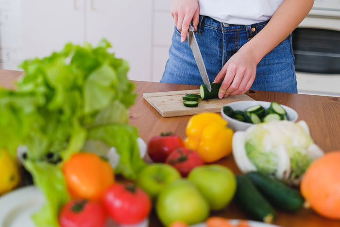 Woman slicing cucumber on a cutting board in kitchen surrounded by fresh vegetables, symbolizing parenting and family dynamics. Woman slicing cucumber on a cutting board in kitchen surrounded by fresh vegetables, symbolizing parenting and family dynamics.