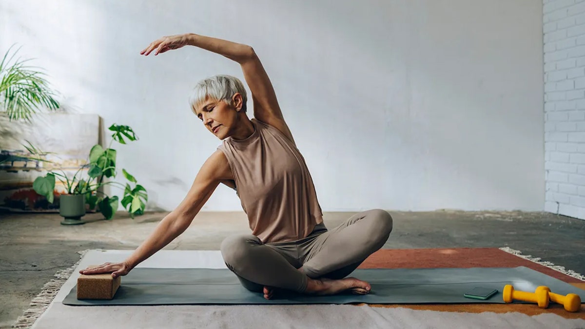 Woman sitting on an exercise mat doing yoga and stretching.
