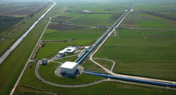 An aerial view of a series of white buildings in the middle of a grassy field connected by dirt roads.