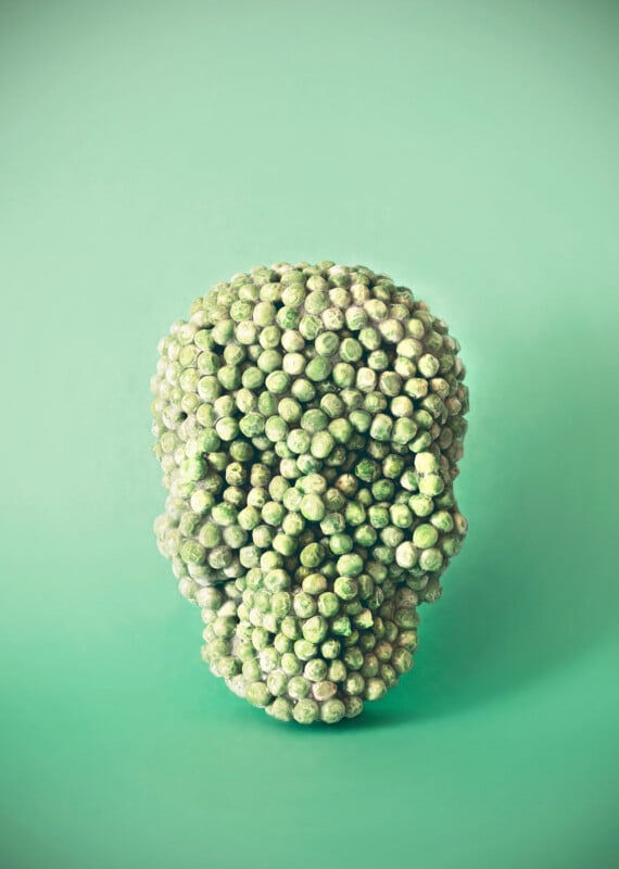 A sculpture of a human skull made entirely of Brussels sprouts is set against a mint green background.