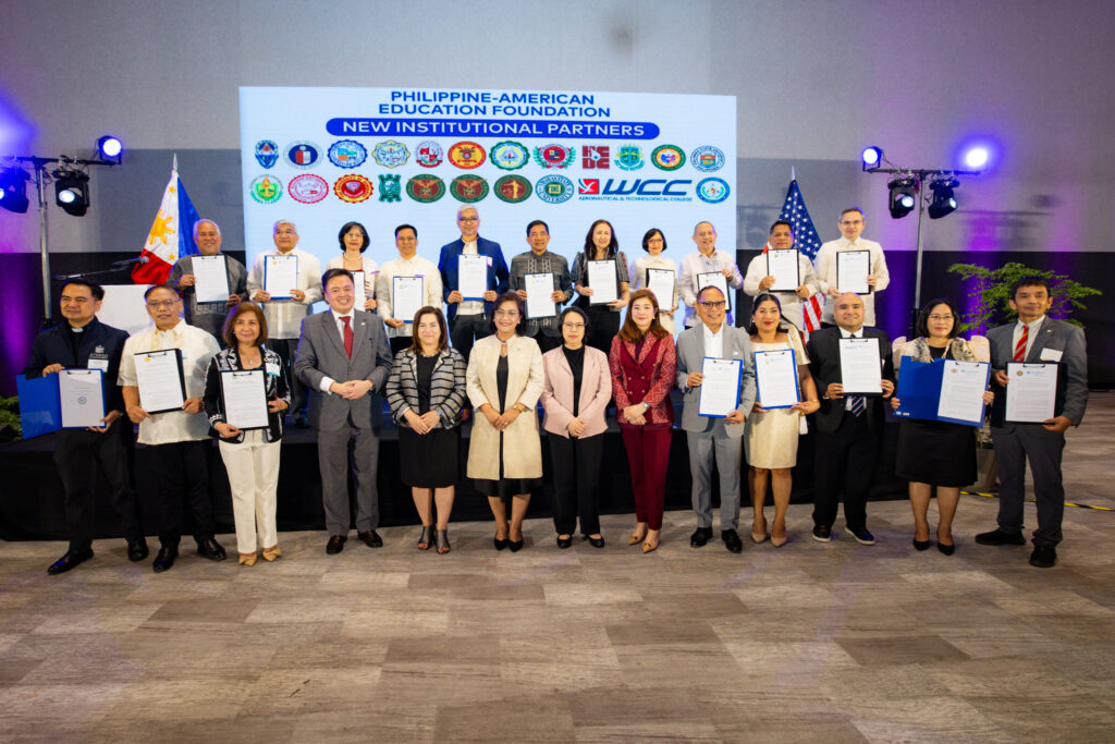 Fulbright Philippines officials and representatives of partner universities standing in front of an LED wall in between the Philippine and U.S. flags.