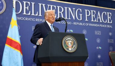 A crane lowers a white package containing food aid into a crate off of the side of a ship.
