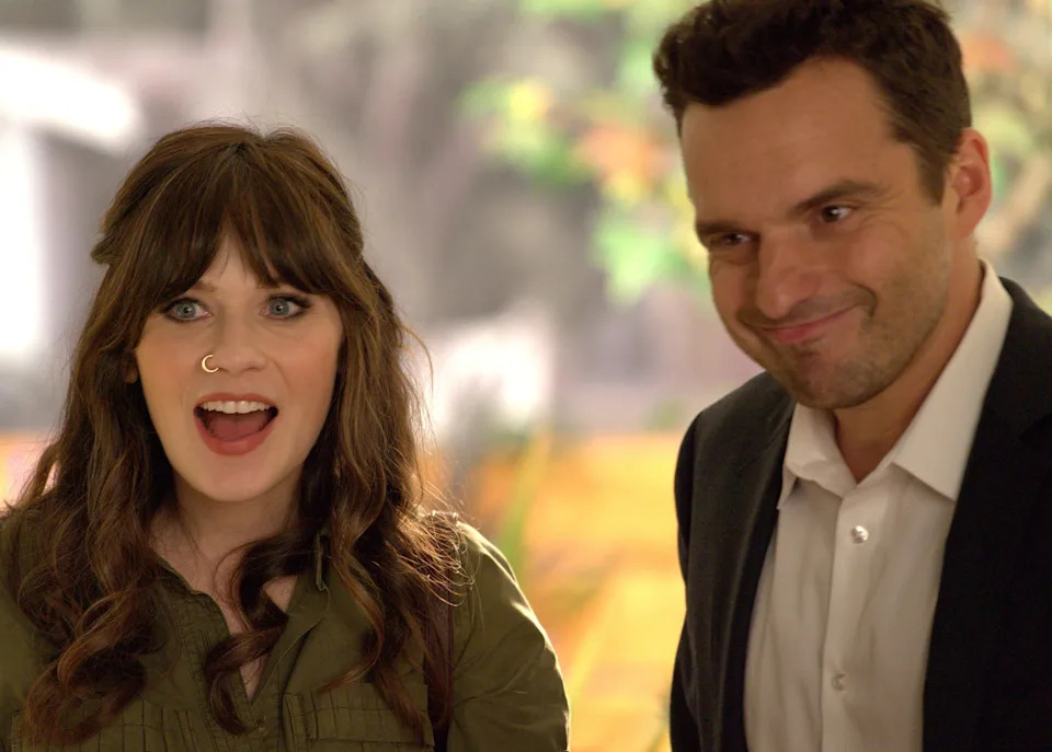 Two people smiling enthusiastically, one with long hair and a nose ring, wearing a casual top; the other with short hair in a suit