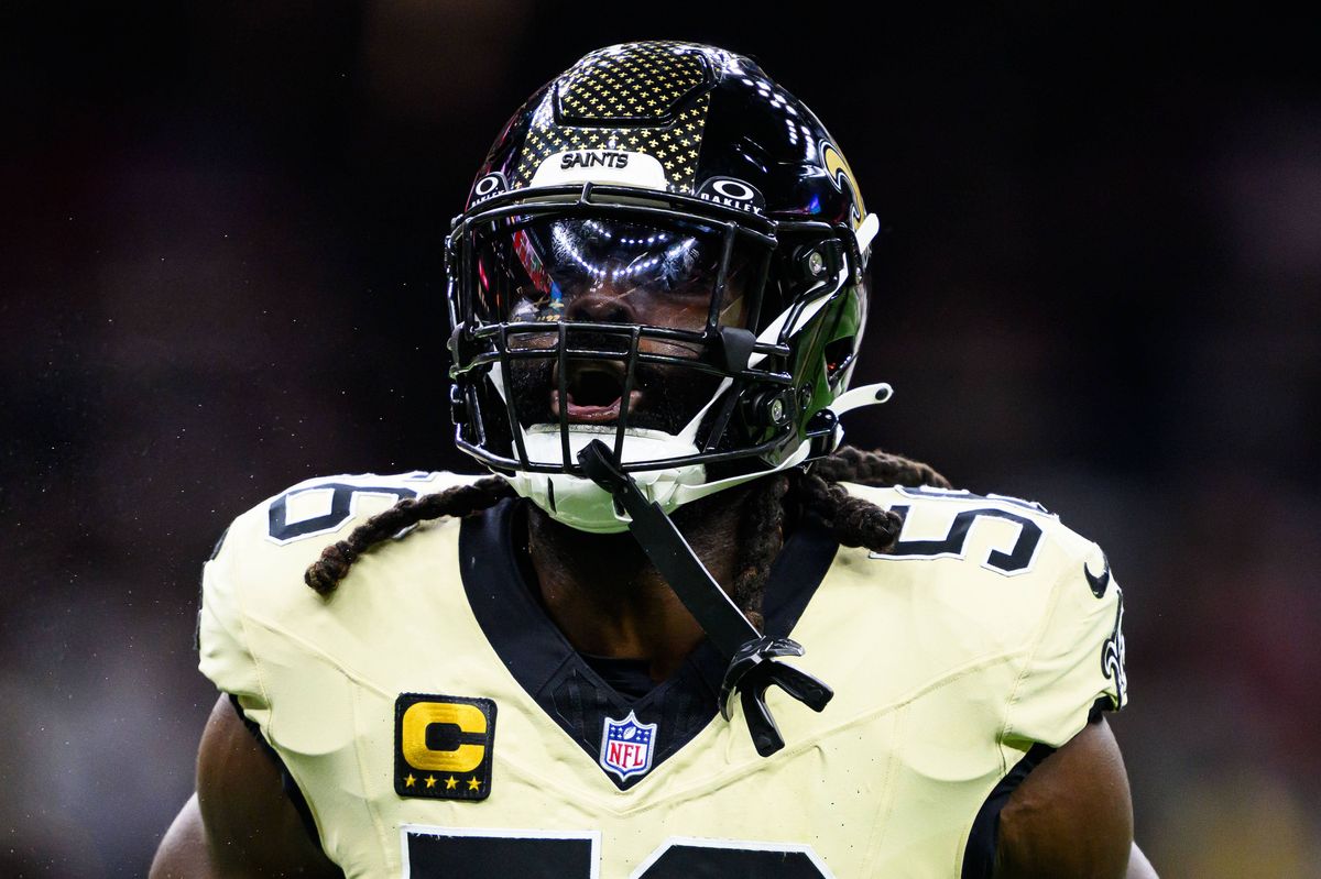 An image depicts a professional football player, clad in a white jersey with the number 56 prominently displayed on the back, standing on the field during a game. The player is wearing a helmet and appears to be focused on the game. The background shows a blurred view of the audience, indicating a lively and engaged crowd.