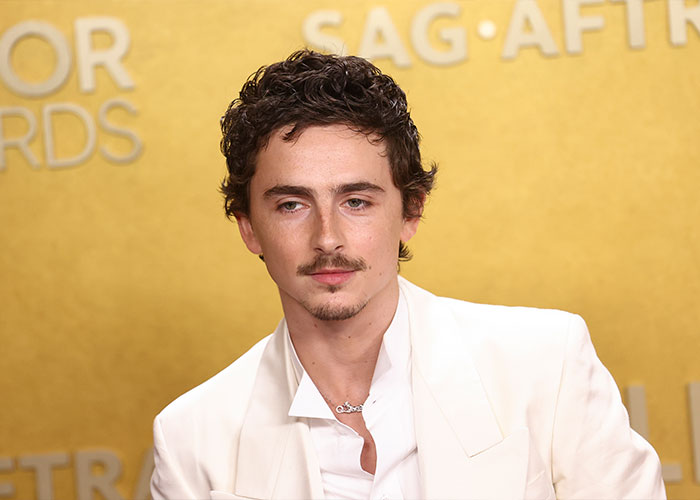 Timothée Chalamet at a SAG Awards event wearing a white suit with a serious expression discussing Oscar chances.