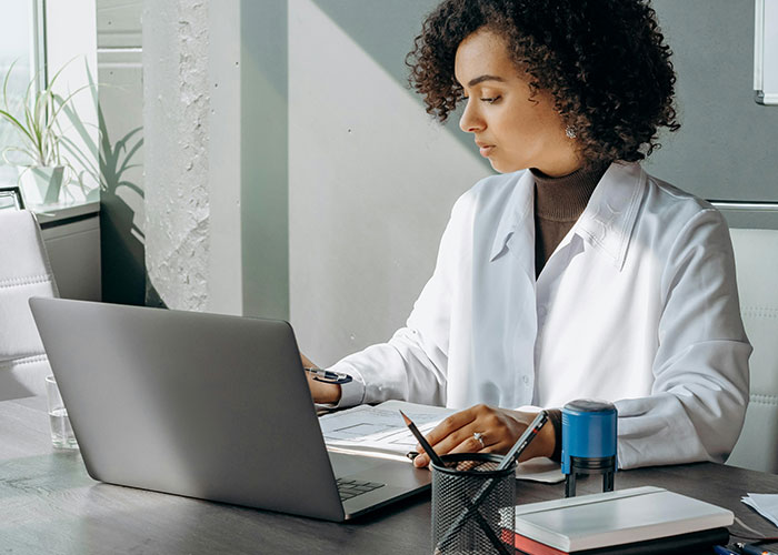Medical professional in a white lab coat working on a laptop, revealing dark medical secrets in a modern office setting.