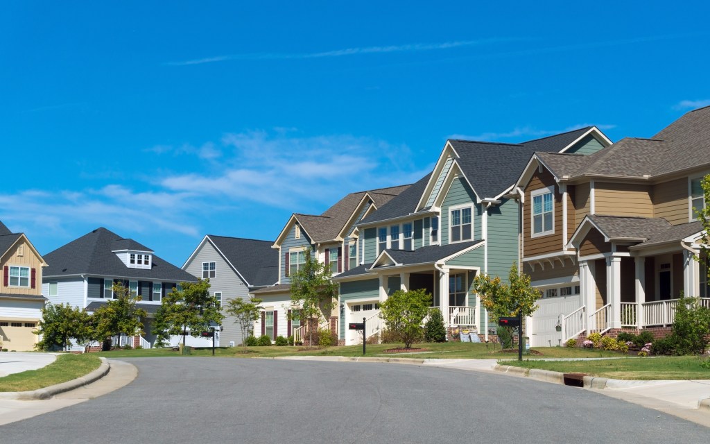 A row of residential houses with varied siding colors and styles lining a curved street in a suburban neighborhood.