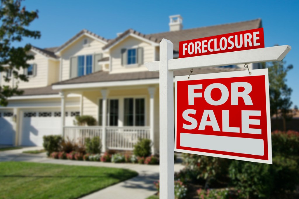 A "Foreclosure For Sale" sign in front of a house.
