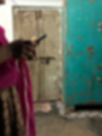 A woman holds her phone in a small, dilapidated room; her face is out of frame.