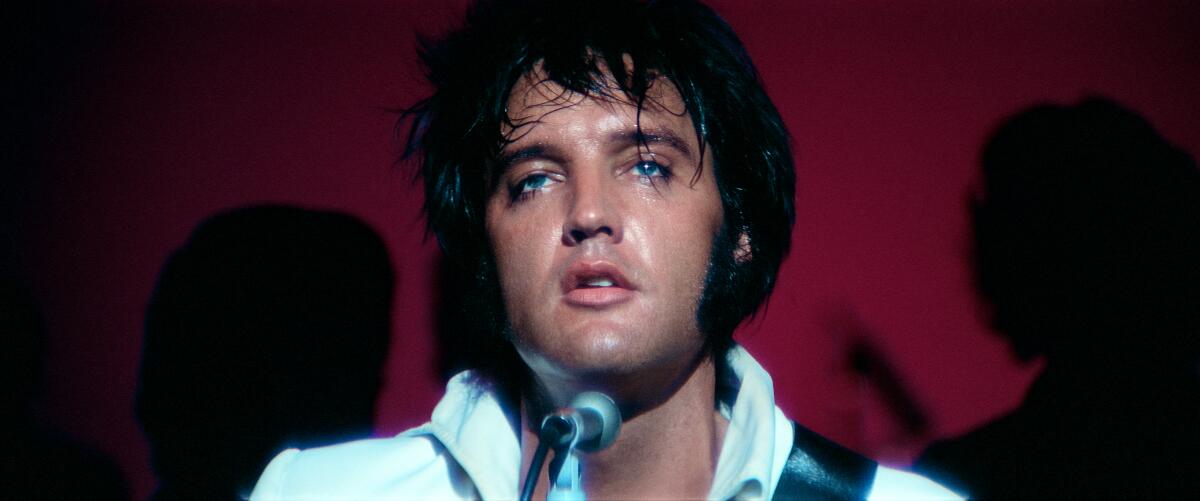 A man with dark hair, sweating, sings before a mic