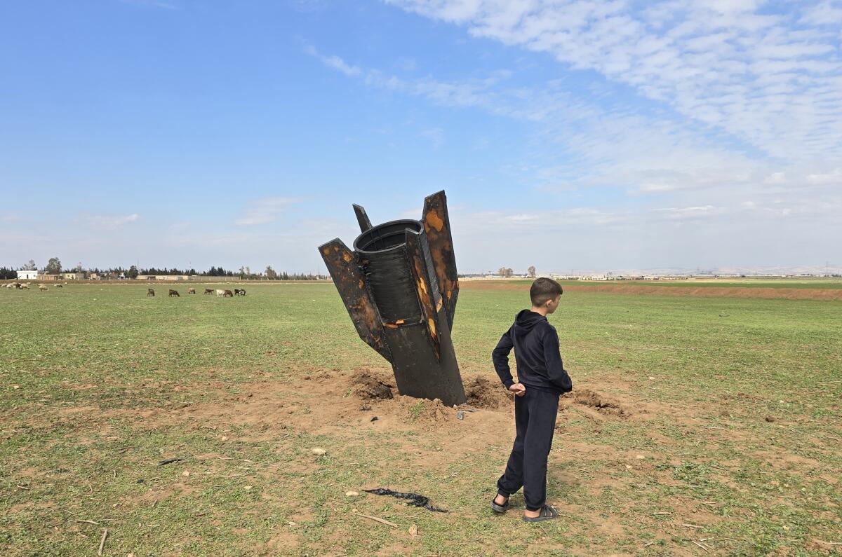 A person in black clothing standing near the tail of a dark missile sticking out of the ground in an open field