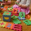 Children play with colorful, numbered puzzle pieces on the floor. Their faces are not visible.