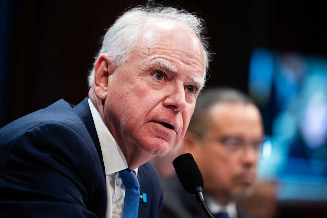 A man wearing a blue suit and tie leans in to speak into a microphone.