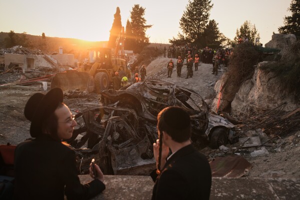 Ultra-Orthodox Jewish men watch as Israeli security forces operate at the site where several people were killed in an Iranian missile strike in Beit Shemesh, Israel, Sunday, March 1, 2026. (AP Photo/Leo Correa)