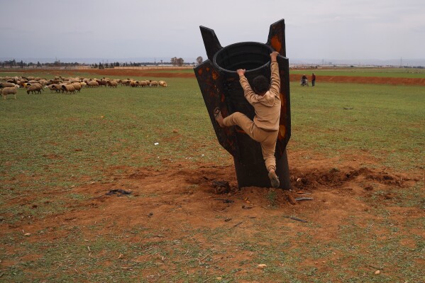 Exposing himself to the danger of unexploded ordnance, a boy tries to climb on an unexploded Iranian projectile that landed in an open field in the outskirts of Qamishli, eastern Syria, Wednesday, March 4, 2026. (AP Photo/Baderkhan Ahmad)