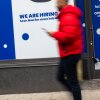 A person walks past a storefront with "we are hiring" and "opening soon" signs out front.
