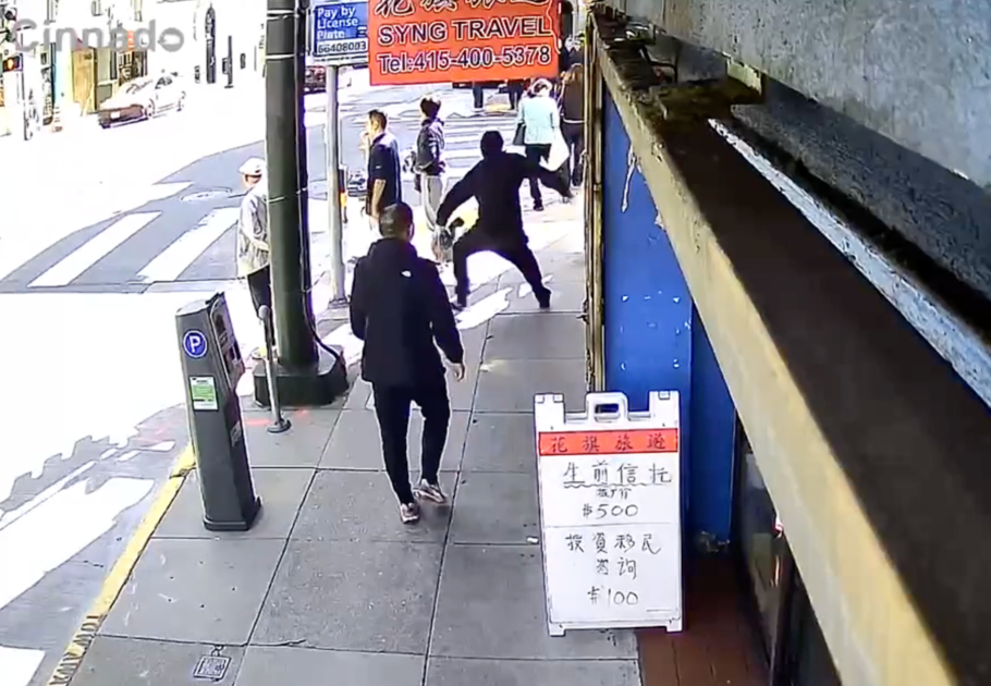 A woman in a burgundy blazer, white top, and black pants stands confidently outside a modern building with large windows reflecting trees.