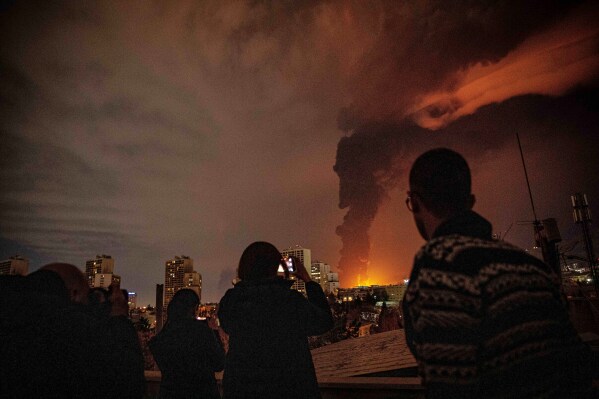 Residents watch and take pictures as flames and smoke rise from an oil storage facility struck as attacks hit the city during the U.S.–Israeli military campaign in Tehran, Iran, Saturday, March 7, 2026. (Alireza Sotakbar/ISNA via AP)