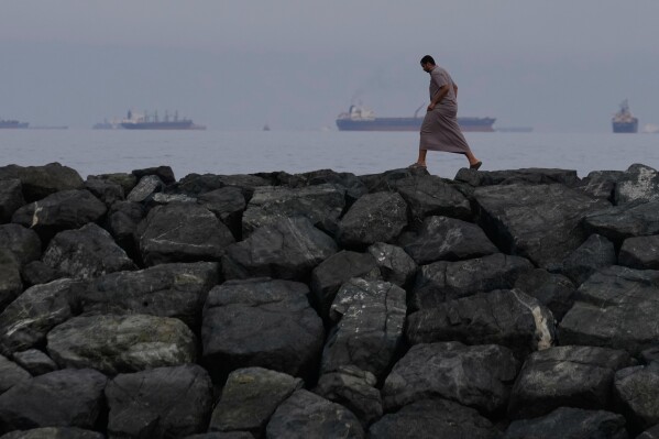 A man walks along the shore as oil tankers and cargo ships line up in the Strait of Hormuz, seen from Khor Fakkan, United Arab Emirates, Wednesday, March 11, 2026. (AP Photo/Altaf Qadri)