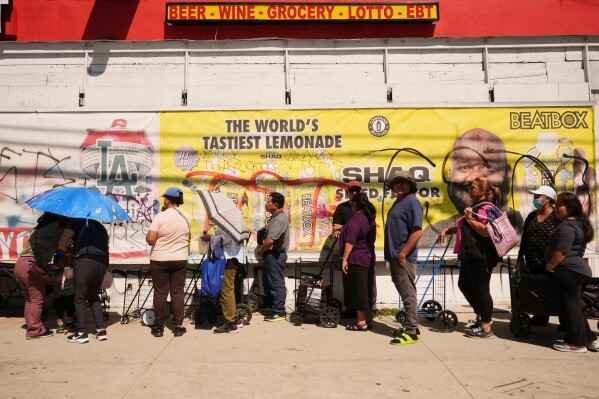 People cover themselves from the heat with umbrellas while waiting at a food distribution site Wednesday, March 11, 2026, in Los Angeles. (AP Photo/Damian Dovarganes)