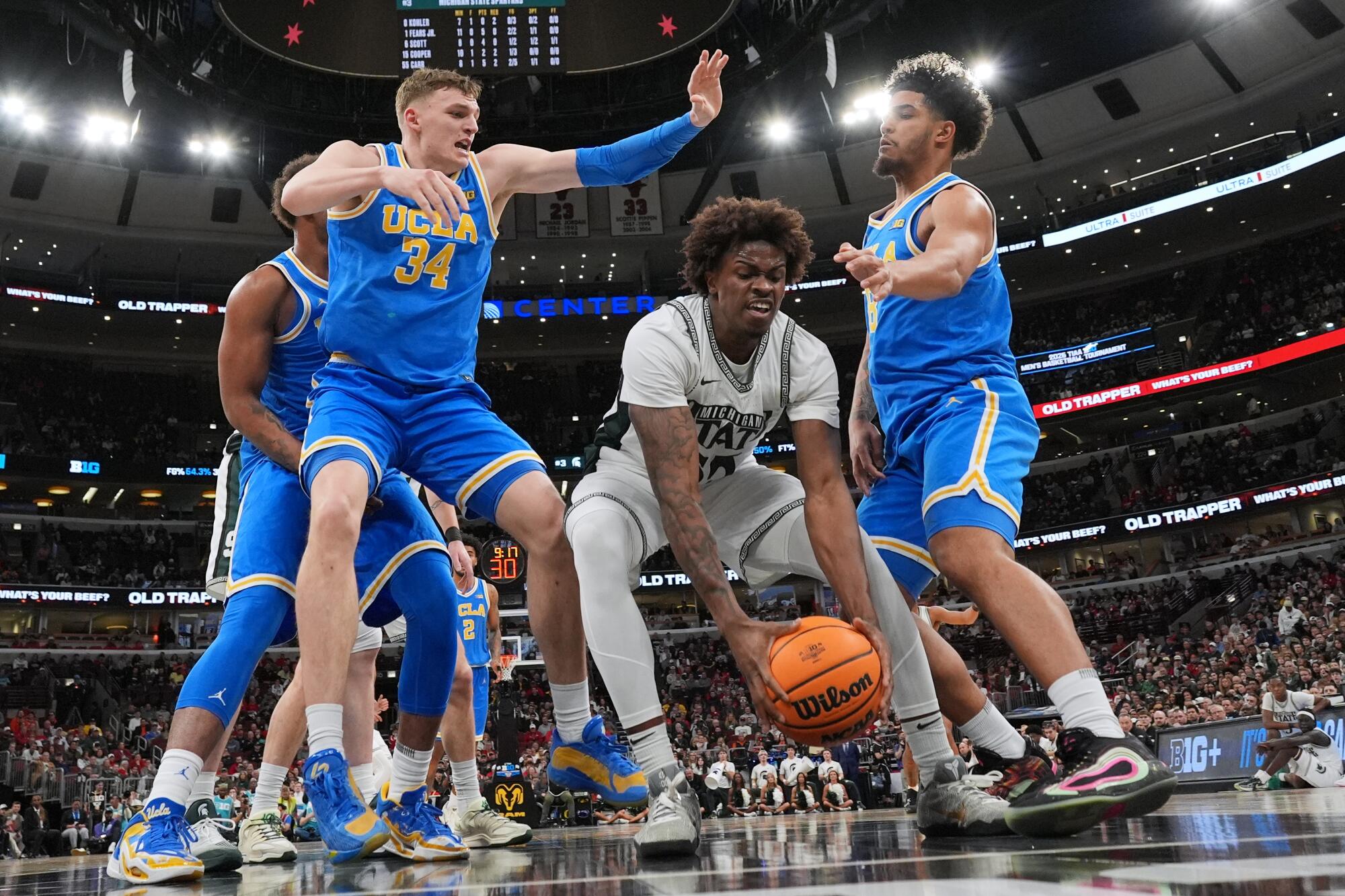 Michigan State forward Coen Carr, center, tries to control the ball between UCLA forward Tyler Bilodeau.