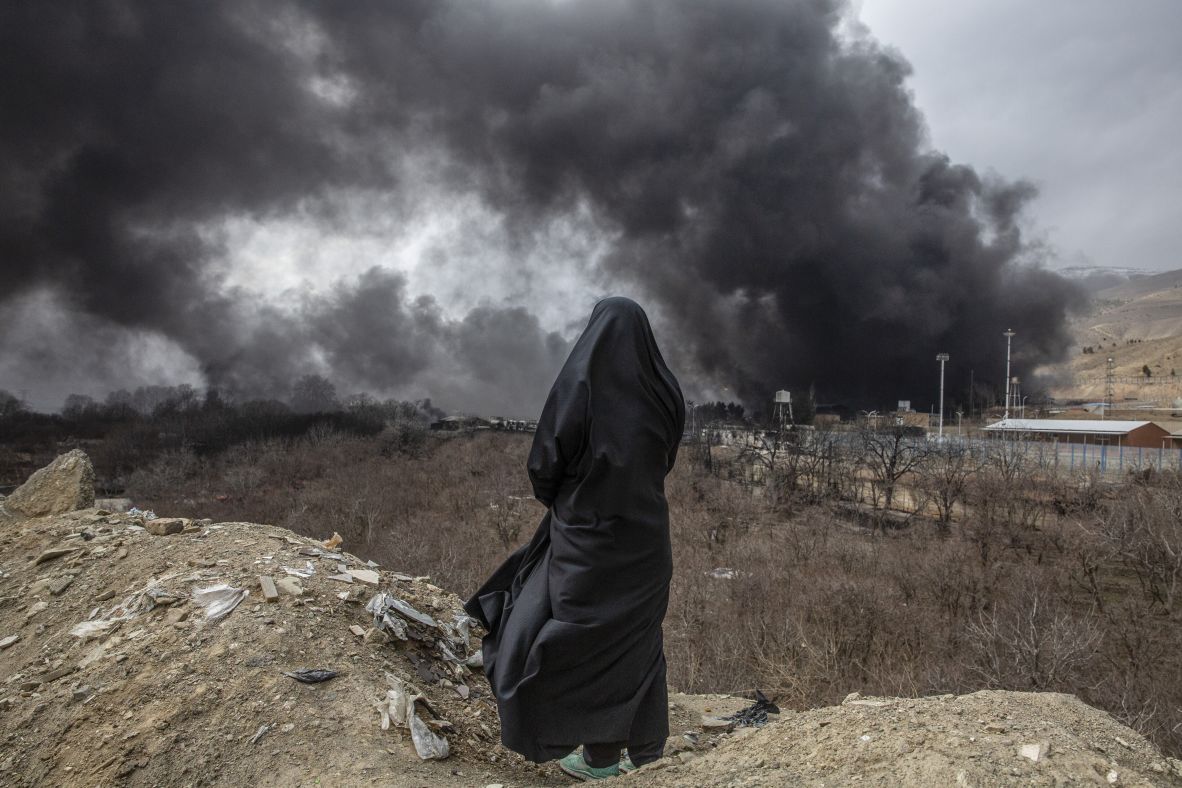 A woman watches plumes of smoke rise from an oil storage facility after overnight strikes in Tehran, Iran, on Sunday, March 8.