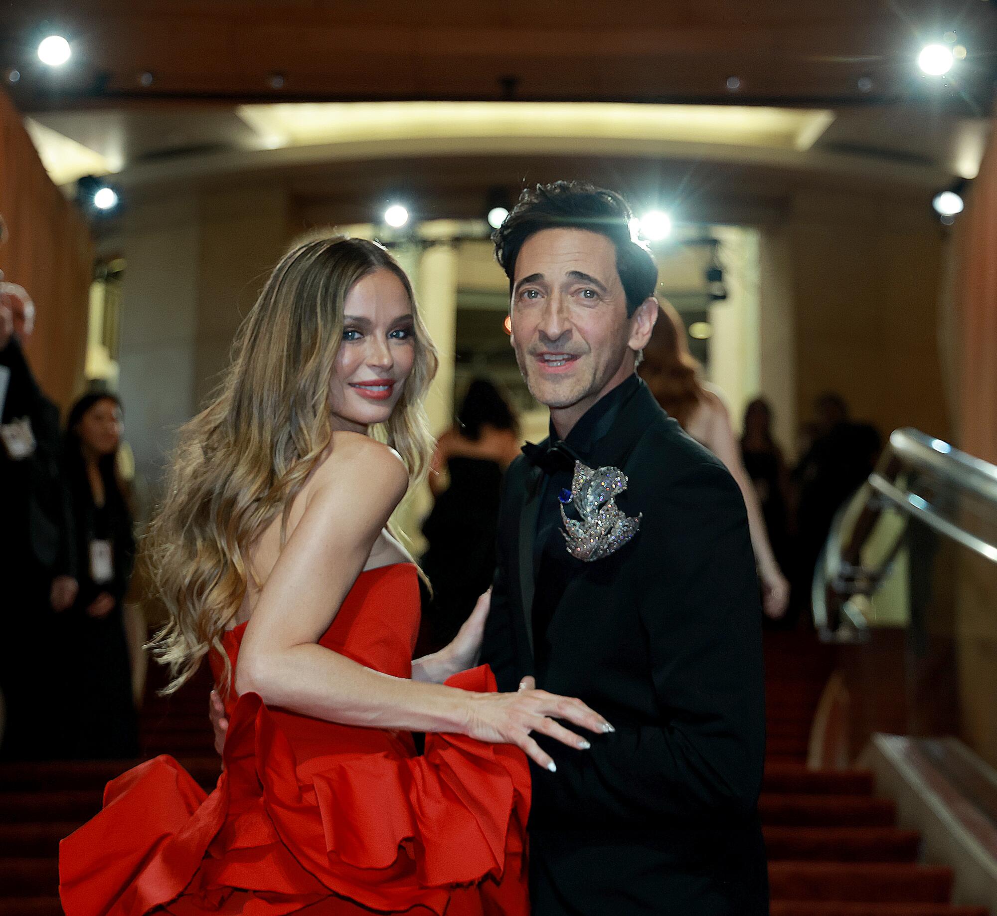 Adrien Brody and Georgina Chapman walk up the stairs on the red carpet.  