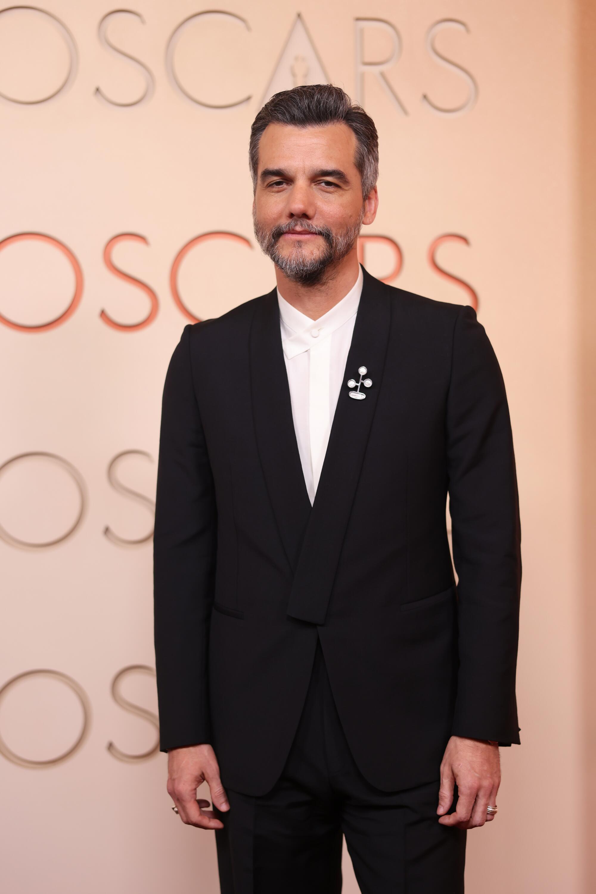 Wagner Moura, wearing a black suit without a tie, poses on the red carpet. 