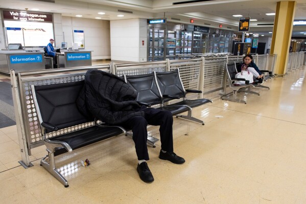 A man sleeps in the baggage claim area of Ronald Reagan National Airport, in Arlington, Va., Monday, March 16, 2026. (AP Photo/Cliff Owen)