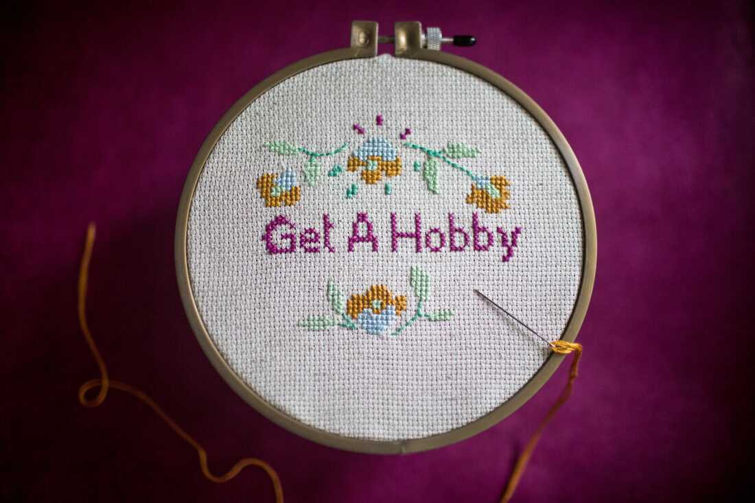 Photograph of cross-stitch ring that reads "Get A Hobby" surrounded by flowers and against a fuchsia background.