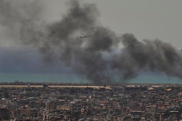 A Middle East Airlines plane takes off from Rafik Hariri International Airport as smoke rises from the site of an Israeli airstrike in Dahiyeh, Beirut's southern suburbs, Lebanon, Tuesday, March 17, 2026. (AP Photo/Hassan Ammar)
