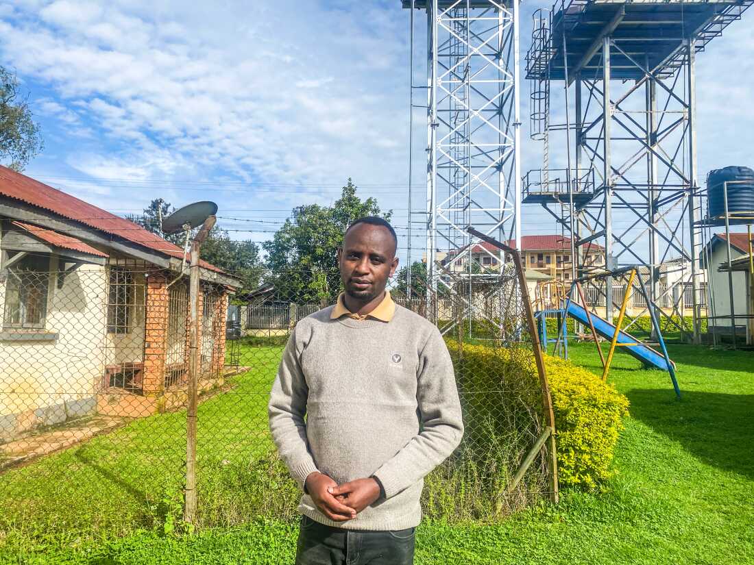 Harerimana Ismail is a community health care worker in Uganda who supports children and teens with HIV. He lost his salary as part of the U.S. aid cuts but still does his job. He's standing outside the hospital where he works.