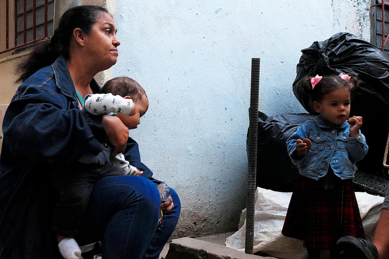 A woman holds an infant as she looks over at a young girl in the room.