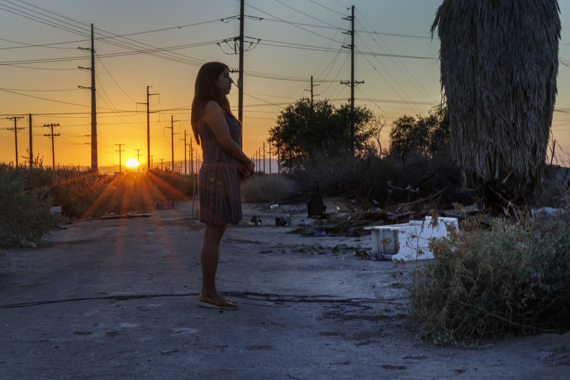 Daniela Flores stands on open land with shrubsn and utility poles in the background