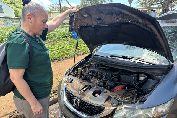 Maile Mills looks under the hood of her car Tuesday, March 24, 2026, after it was damaged by flood waters in Honolulu. (AP Photo/Audrey McAvoy)