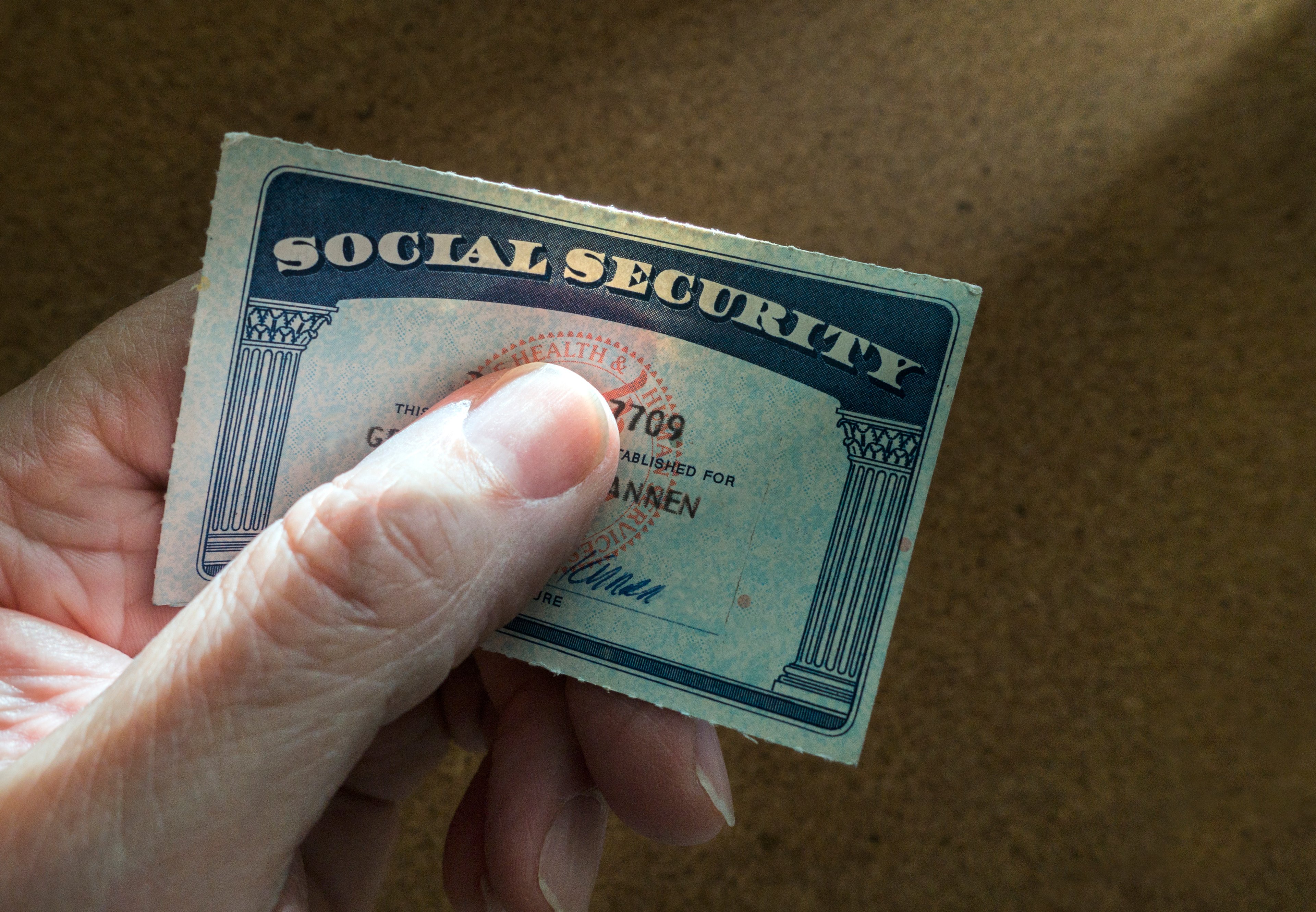 A hand is shown, holding a Social Security card.