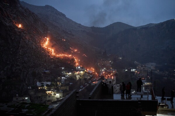 Kurdish people carry lit torches as they walk up a hill overlooking Akra in the autonomous Kurdistan Region of Iraq, Friday, March 20, 2026, during celebrations for Nowruz, Persian New Year. (AP Photo/Leo Correa)