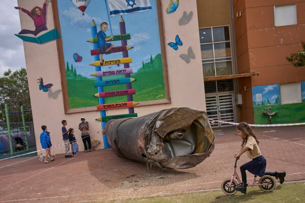 Children play beside a fragment of an Iranian ballistic missile that landed in a schoolyard in the Israeli settlement of Peduel in the West Bank, Monday, March 23, 2026. (AP Photo/Ohad Zwigenberg)