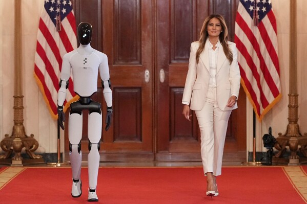 First lady Melania Trump, accompanied by a robot, arrives to attend the "Fostering the Future Together Global Coalition Summit" at the White House, Wednesday, March 25, 2026, in Washington. (AP Photo/Jacquelyn Martin)