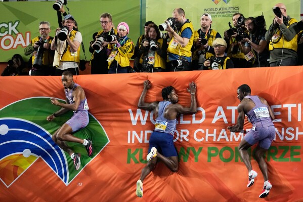 Jordan Anthony, of the United States, Jeremiah Azu, of Britain, and Trayvon Bromell, of the United States, from left, jump into the mat after the men's 60 meters final at the World Athletics Indoor Championships in Torun, Poland, Friday, March 20, 2026. (AP Photo/Matthias Schrader)