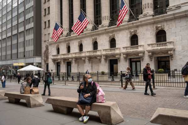 People sit on benches outside the New York Stock Exchange, Friday, March 27, 2026, in New York. (AP Photo/Yuki Iwamura)