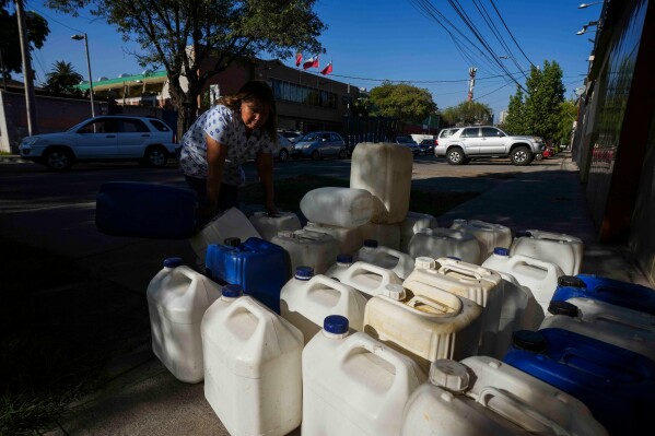 A woman sells cartons for fuel as drivers line up to fill their tanks with gas in Santiago, Chile, Tuesday, March 24, 2026. (AP Photo/Esteban Felix)