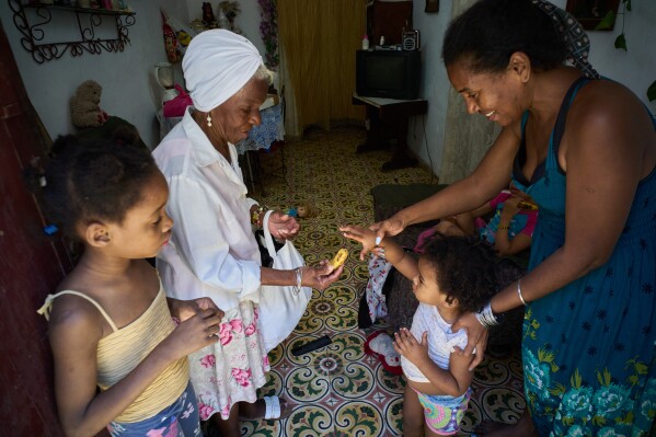 Yuneisy Riviaux helps her daughter Seinet to reach for a banana from a friend at their home in Havana, Cuba, Wednesday, March 25, 2026. (AP Photo/Ramon Espinosa)